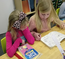 two children sat at a table reading a book together