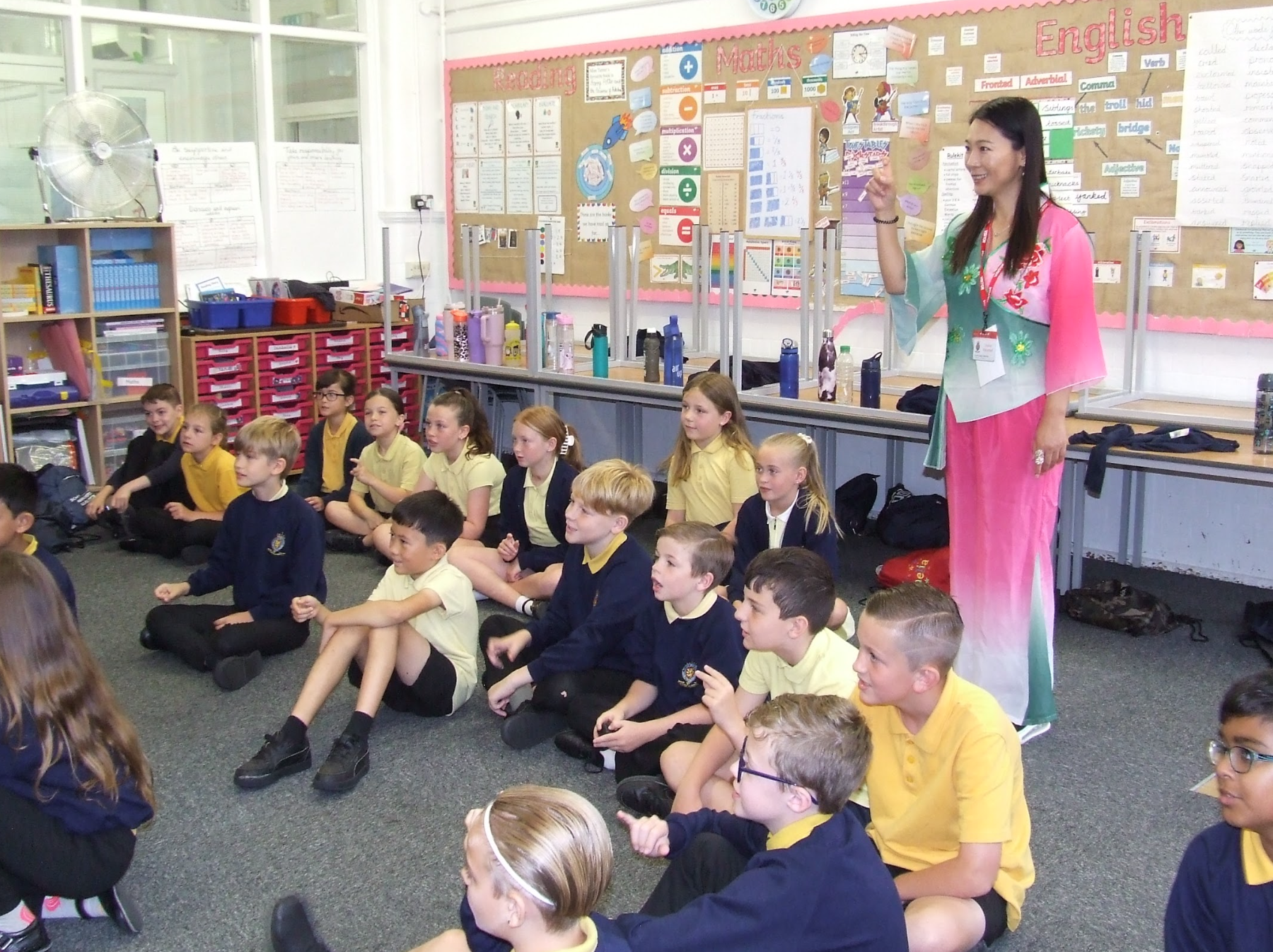 Children sat on floor in classroom with an adult standing