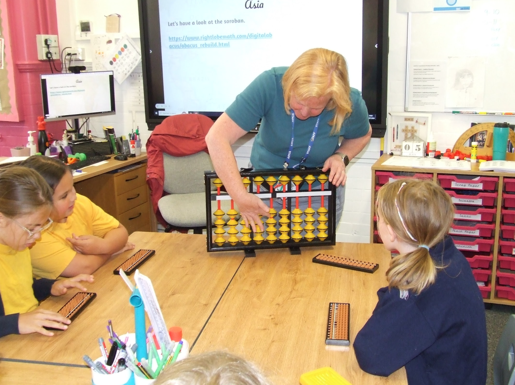 children sat at a table watching a teacher demonstration